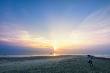 Fototapeta premium Asian woman tourist taking photo on the beach and beautiful natural landscape of colorful sky and sea during a sunset at Nathon Sunset Viewpoint in Samui island, Surat Thani, Thailand