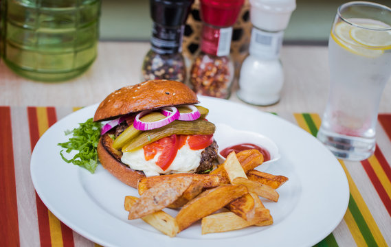 Horizontal color image of Beef Burger with french fries on a white plate on a restaurant table. 