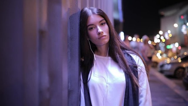 Woman listening to music and relaxing leaning at wall in night city