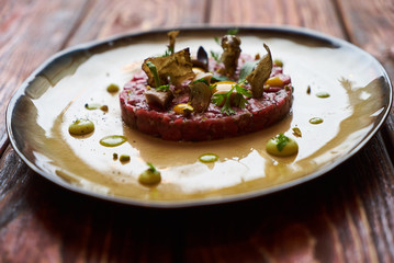 Beef tartare Steak with egg yolk, pistachios, truffle oil, green mayonnaise on porcelain plate. Classic tartare meat with ingredients. Luxury food