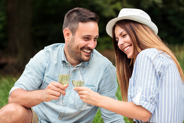 Happy young couple celebrating anniversary or birthday by having a romantic picnic in park. Making a toast with white wine. Love, dating, romance and lifestyle concept