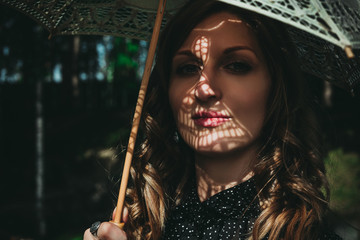 Portrait of an young woman under white umbrella with shadows of lace on her face