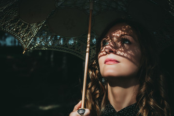 Portrait of an young woman under white umbrella with shadows of lace on her face