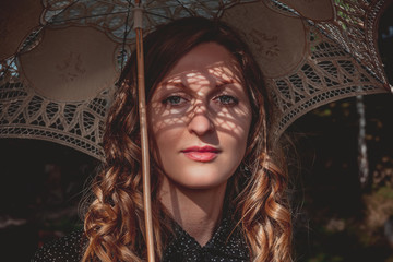 Portrait of an young woman under white umbrella with shadows of lace on her face
