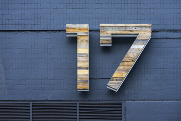 Wooden number seventeen on blue brick wall with ventilation grilles