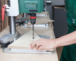 Close up. Carpenter at work using vertical drilling machine. Workshop.