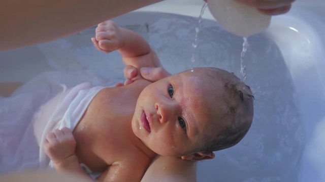 Newborn baby bathed by mother in tub. Squeezing water from sponge on newborn babies head.