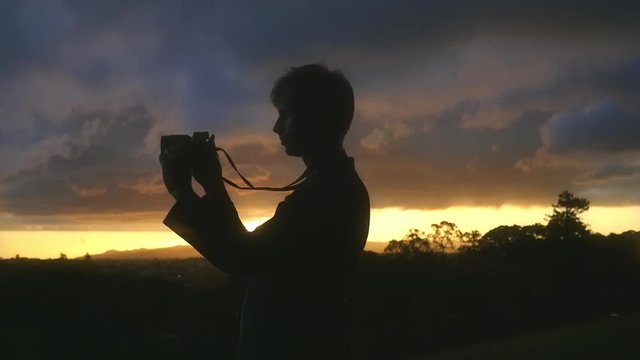 Man silhouette against streaking orange sunset lifting camera to take photos.