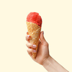 Female hand with a horn of strawberry ice cream on a light pink background