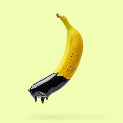 Banana with dripping black paint on yellow background. Creative food concept.