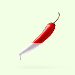 Red pepper with dripping white paint on light green background. Creative food concept