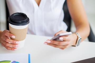 Young woman using her phone and drink coffee in office