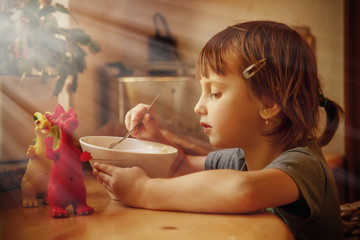 Little cute child girl eating noodles with dragon toys