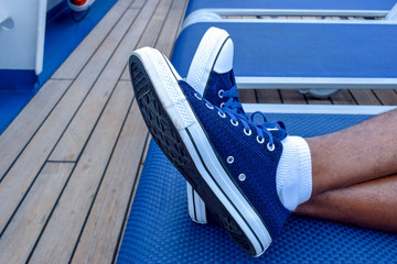 Feet crossed. Blue sneakers laced up. White socks. Lounge chair. Resting. Relaxing. Vacation. Man....