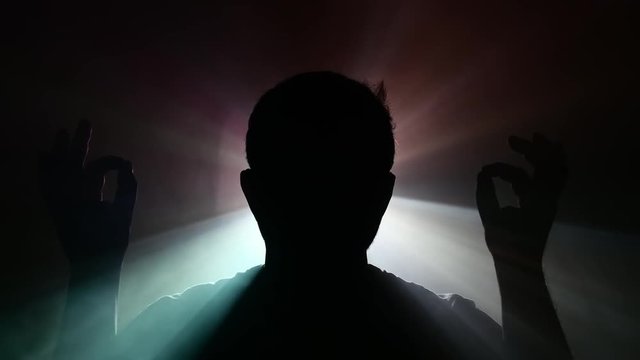 man doing meditation with enlighting glow - foggy background with a projectior lightsource in the distance