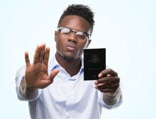 Young african american man holding australian passport with open hand doing stop sign with serious and confident expression, defense gesture