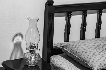 Vintage flat-wick Kerosene Oil Lamp on bedside table, bed headboard, pillow, mattress, bedroom.