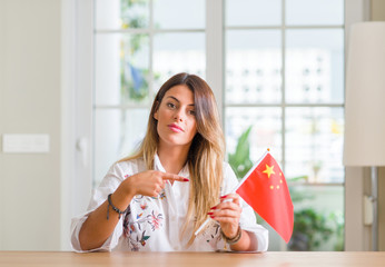 Young woman at home holding flag of China very happy pointing with hand and finger
