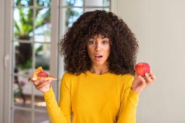 African american woman choosing between apple and pizza slice scared in shock with a surprise face, afraid and excited with fear expression