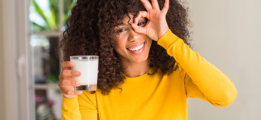 African american woman holding a glass of milk with happy face smiling doing ok sign with hand on eye looking through fingers