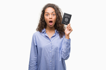 Young hispanic woman holding passport of Italy scared in shock with a surprise face, afraid and excited with fear expression