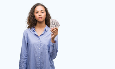 Obraz premium Young hispanic woman holding dollars with a confident expression on smart face thinking serious