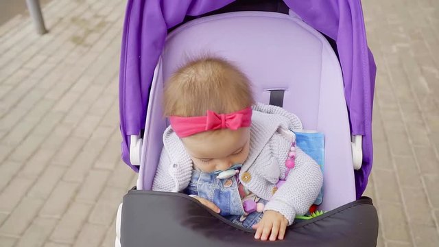 Close up shot of a cutests little girl sitting in a stroller with a pacifier in her mouth.