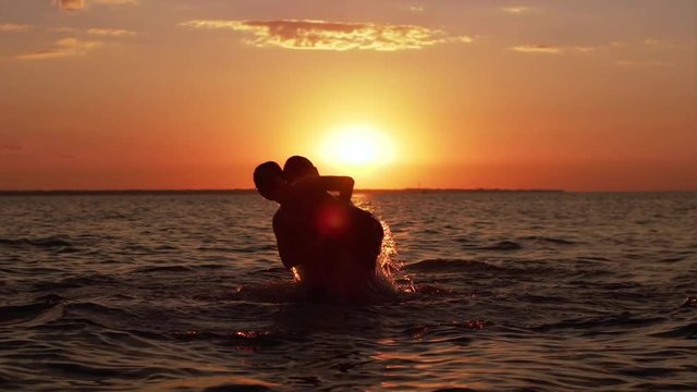 Silhouettes of adult man swimming and throwing little boy in air, while having fun in sea during beautiful sunset in slow motion
