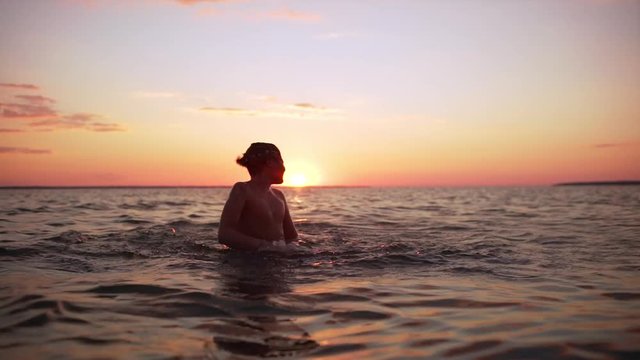 Portrait of young european boy 10-12 diving and swimming in sea alone, during amazing dusk in slow motion