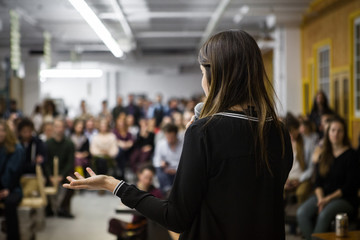 Woman gives a public speech in front of 200 people, in an industrial environment - obrazy, fototapety, plakaty