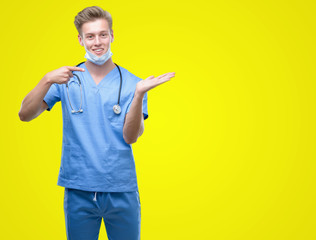 Young handsome blond doctor very happy pointing with hand and finger