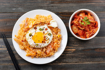 Kimchi fried rice with fried egg on top and fresh kimchi cabbage in a bowl on wooden background, top view, Korean food