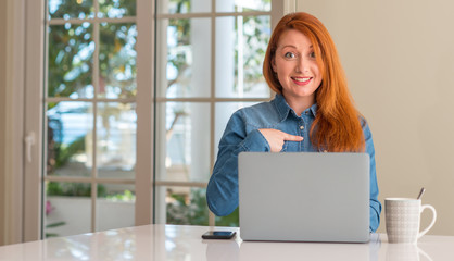 Redhead woman using computer laptop at home with surprise face pointing finger to himself