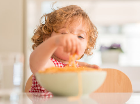 Beautiful child eating spaghetti with hands at home