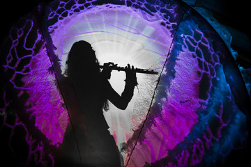 Very sharp shadow of a woman playing flute casted on a psychedelic projection background