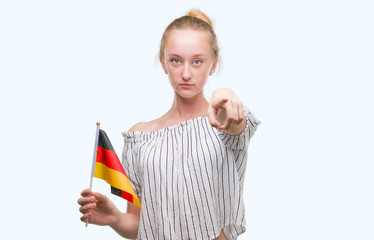 Blonde teenager woman holding flag of Germany pointing with finger to the camera and to you, hand sign, positive and confident gesture from the front
