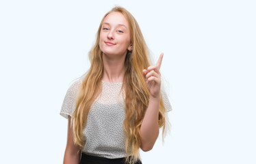 Blonde teenager woman wearing moles shirt showing and pointing up with finger number one while...