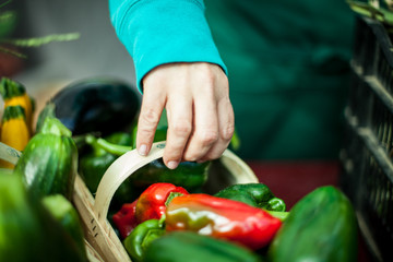 Woman picking up a basket of green and red peppers at farmer's market