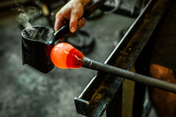 Glass-blower man working with hot orange glass to make a blown glass lantern