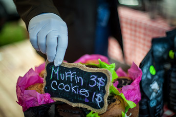 Hand with glove putting a price sign on a muffins and cookies tray at farmer's market