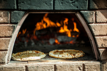 Two handmade pizzas being cooked in a bread oven at farmer's market