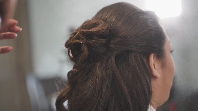 A stylist sprays hairspray on a formal half-up, half-down hairdo and pats into place, Closeup from behind