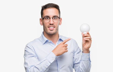 Handsome young man holding lightbulb as idea very happy pointing with hand and finger