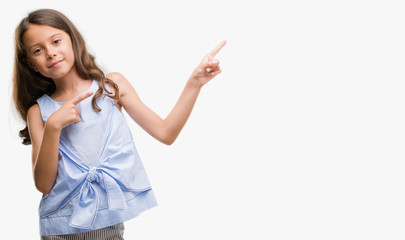 Brunette hispanic girl smiling and looking at the camera pointing with two hands and fingers to the side.