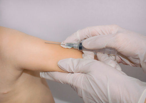 Doctor giving a child an intramuscular injection in arm. Vaccination of children.