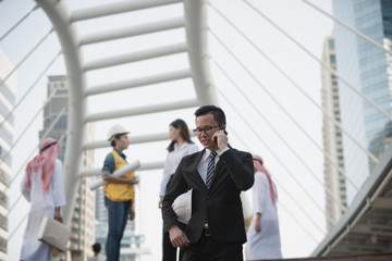 ..Portrait of a young asian businessman talking on mobile phone and holding a helmet. Man outdoor with phone in community sources at city Bangkok Thailand. Concept of communication.