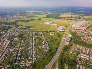 Helicopter drone shot. View from above on a small village, motor road, green forest and a large field on a warm, sunny summer day