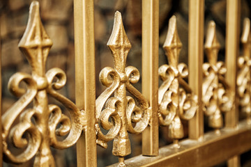 New gold wrought fence close-up background. Forged ornate beautiful pattern golden security bars