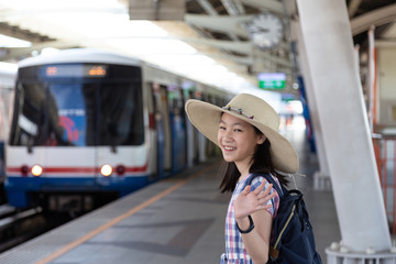 Asian cute girl waving goodbye before go to travel  at skytrain station for travel in the big city,lifestyle and transportation concept