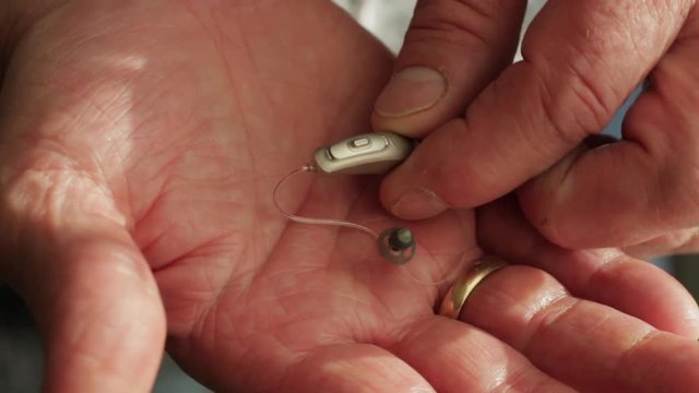 Close up of hearing aid being inspected in the palm of a mans hand. Nano technology used in hearing device for the elderly. Battery powered micro hearing aid.
